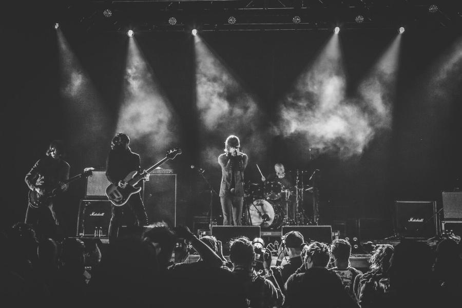 Banda de rock se apresentando ao vivo em um show, com guitarrista, baixista, vocalista e bateria no palco sob luzes coloridas